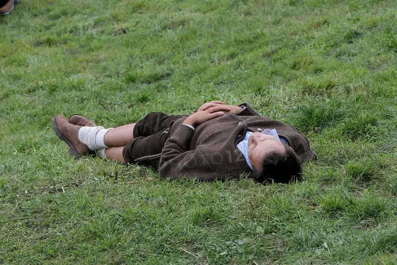 Young man in Bavarian traditional costume sleeps off intoxication from Oktoberfest on lawn