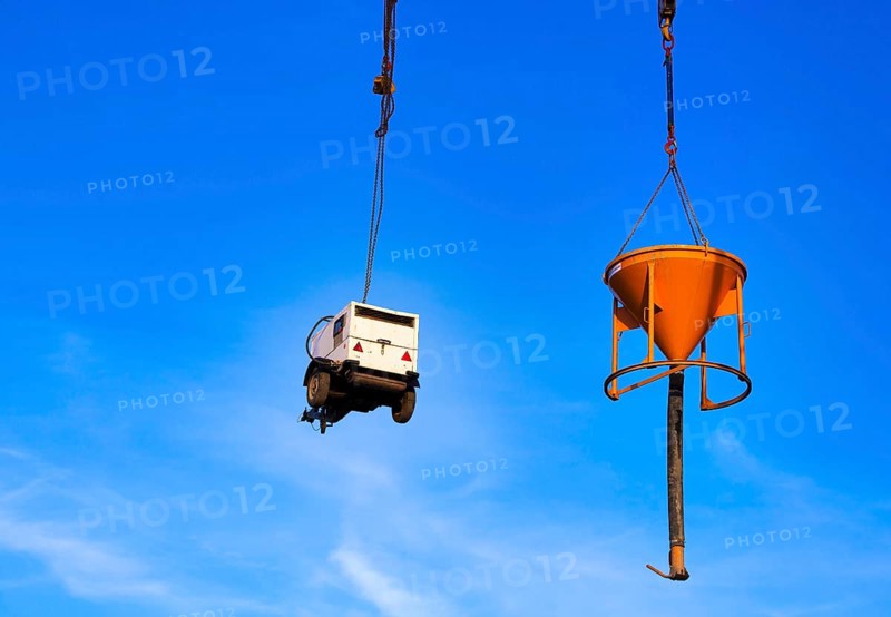 Construction machinery chained to a construction crane against a blue sky