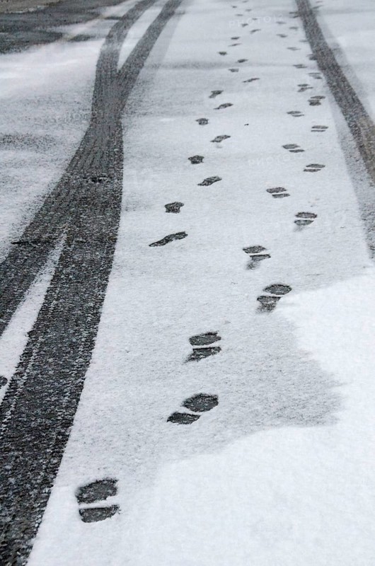 Traces of car tyres and footprints on thin snow cover of asphalt road