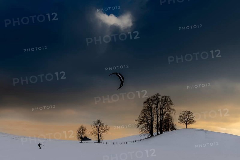 Kite surfers in winter landscape in front of dramatic sky