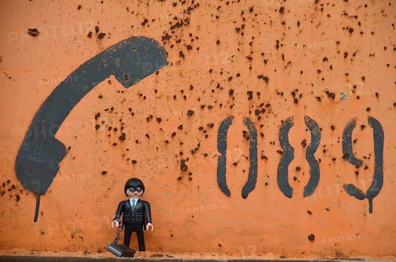 Black figure with telephone receiver and area code of Munich painted on orange metal container