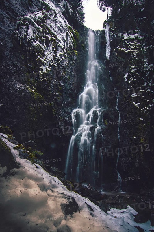 The Burgbach waterfall with snow in winter. Waterfall with stone steps in Schapbach