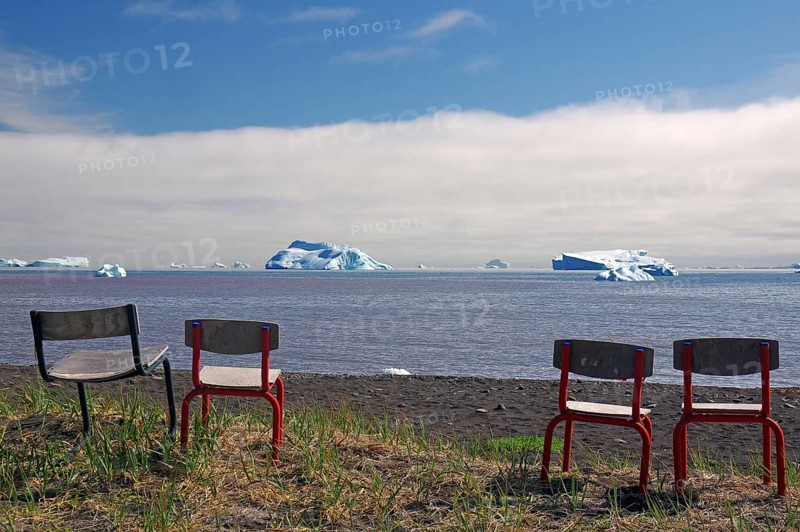 Chairs standing in front of a bay with icebergs floating in it