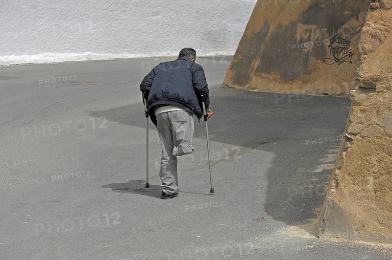 Disabled one-legged man on crutches walks in the street