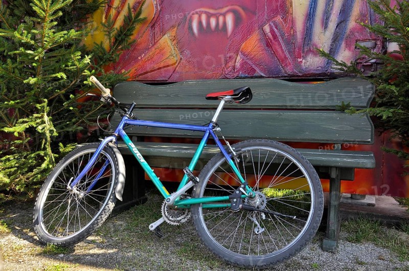 Bicycle leaning against green bench with vampire teeth in the background at Oktoberfest