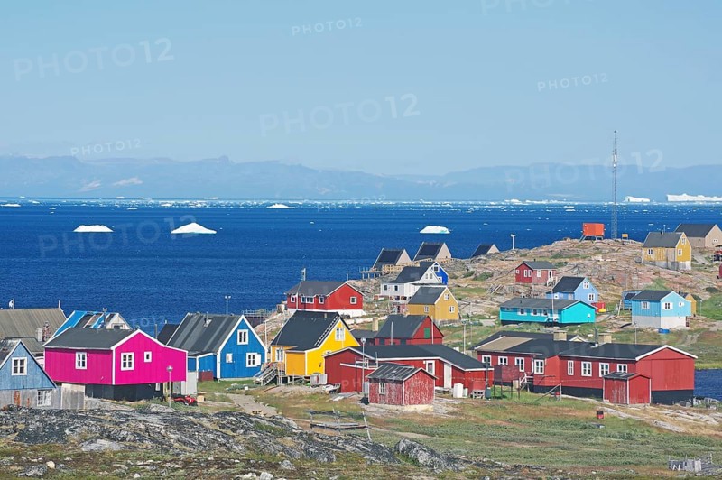 Different coloured wooden houses in front of the bay with icebergs
