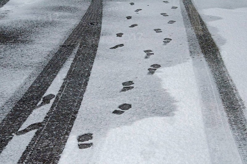 Black tracks from car tyres and footprints in the snow on asphalt road