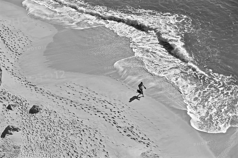 Man with guitar on lonely beach with footprints in sand