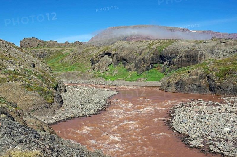 Reddish brown river flowing through a green arctic landscape