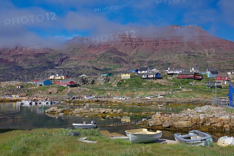 Small boats lie in front of houses and red volcanic mountains