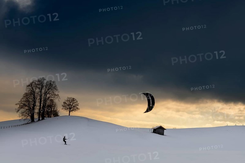 Kite surfers in winter landscape in front of dramatic sky