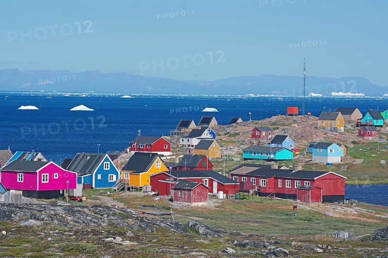 Different coloured wooden houses in front of the bay with icebergs