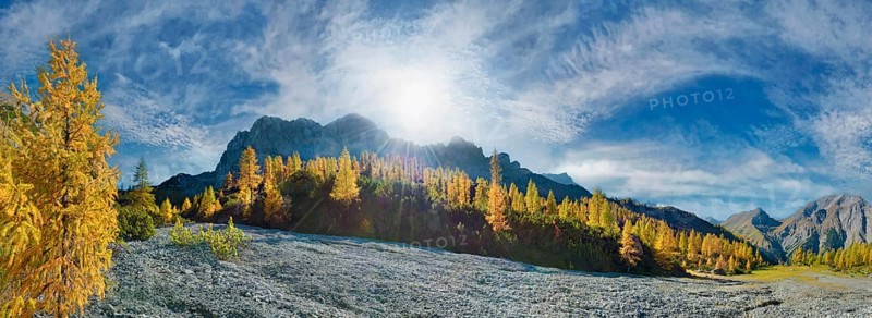 Glowing autumnal mountain forest below the Lamsenjoch massif with bizarre cloudy sky