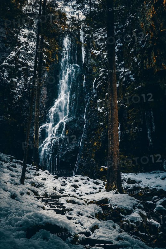 The Burgbach waterfall with snow in winter. Waterfall with stone steps in Schapbach