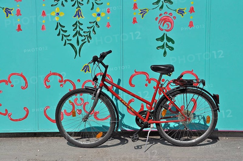 Red bicycle on stand in front of green painted wall with ornaments at Oktoberfest