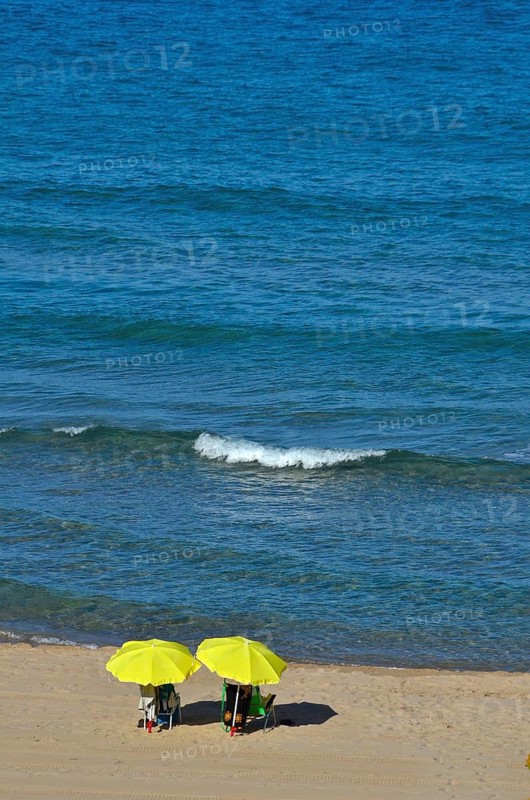 Beachgoers under yellow umbrellas by the sea with wave