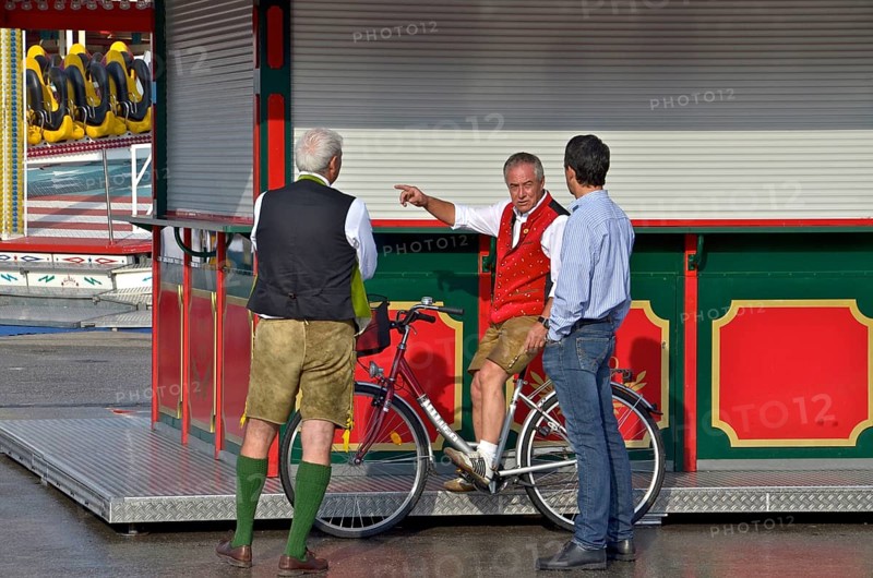 Men in lederhosen chatting with showman at deserted Oktoberfest in front of it begins