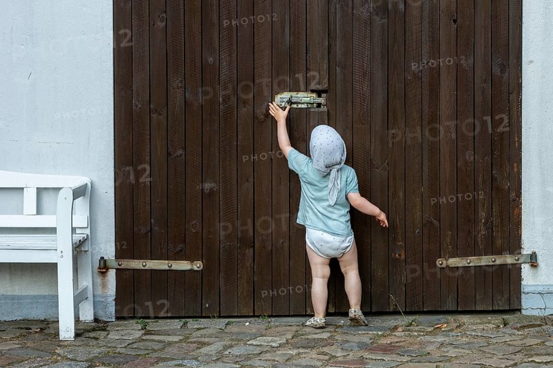 Toddler tries to move the security latch on a wooden door