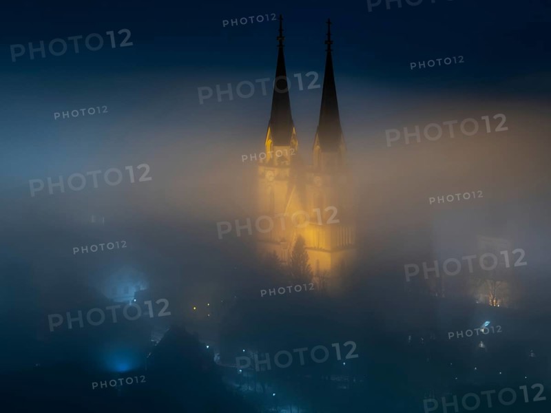 Illuminated church towers of Admont Abbey rise out of the fog