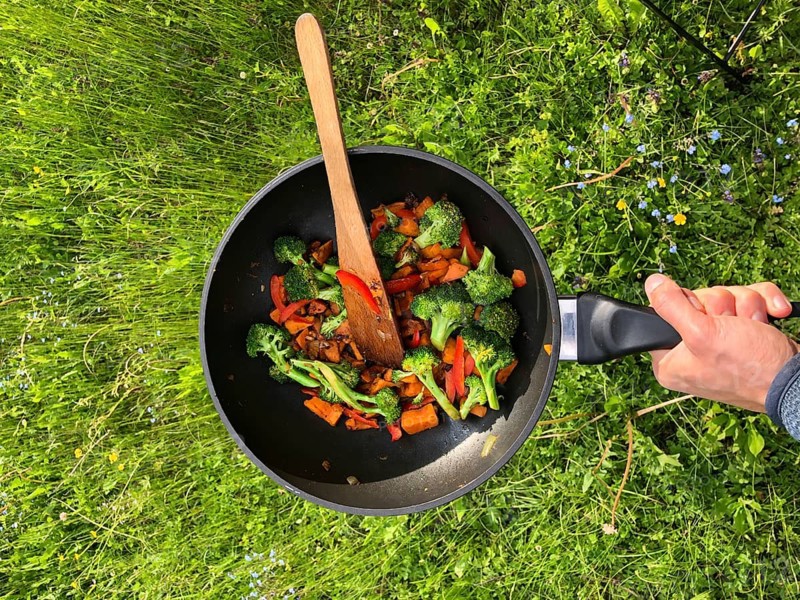 Hand holding pan with fried vegetables