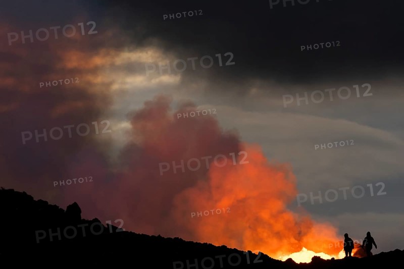 Tourists in front of reddish illuminated smoke cloud