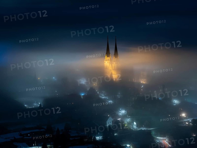 Illuminated church towers of Admont Abbey rise out of the fog
