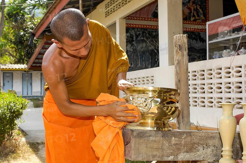 Buddhist monk cleans golden offering bowl in Buddhist monastery