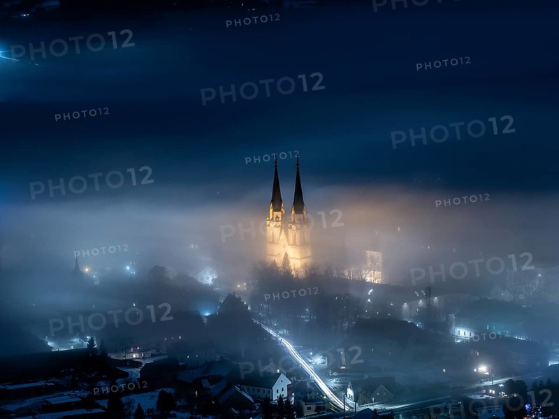 Illuminated church towers of Admont Abbey rise out of the fog