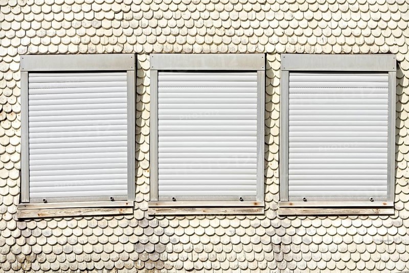 Closed plastic roller shutters in wooden historic facade made of wooden shingles