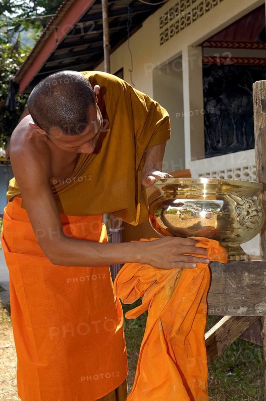 Buddhist monk cleans golden offering bowl in Buddhist monastery