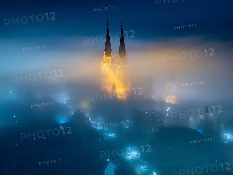Illuminated church towers of Admont Abbey rise out of the fog