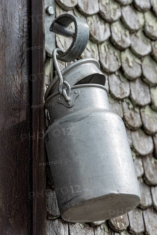 Old aluminium milk can hangs on house entrance of historic clapboard house