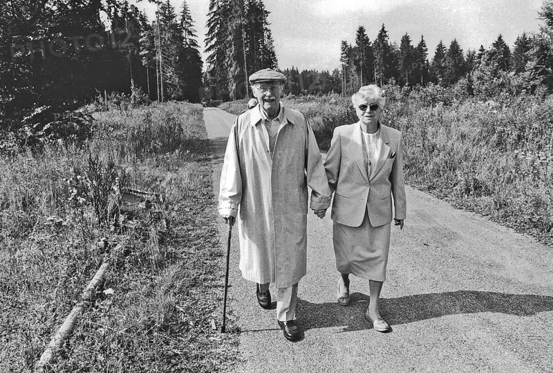 Old couple walking hand in hand on forest path