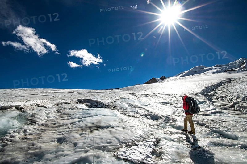 A climber with crampons and backpack walks across the sunlit Mera Glacier