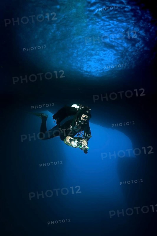Diver dives with underwater lamp through rock grotto with blue light Blue Dome in Blue Hole of Gozo