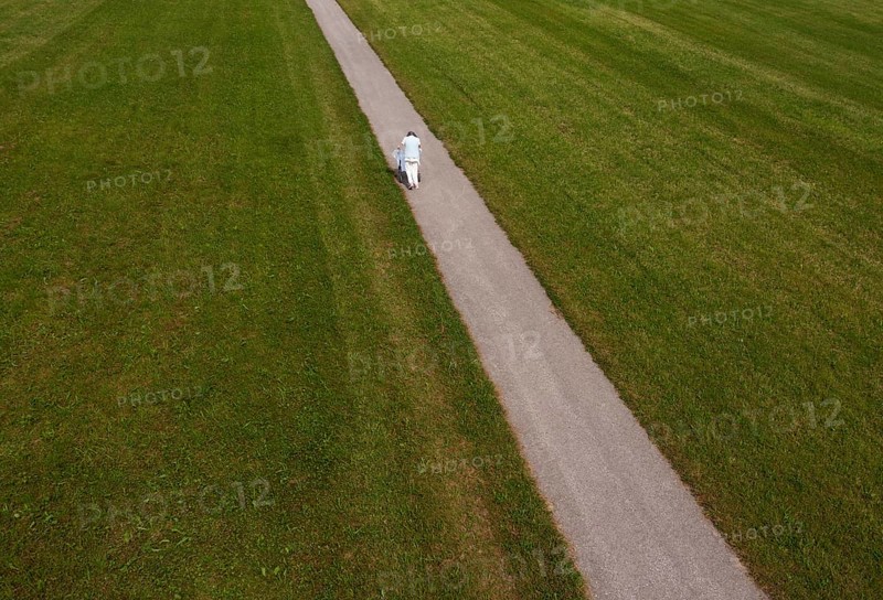 Frail woman walking with a Rolator along a narrow path
