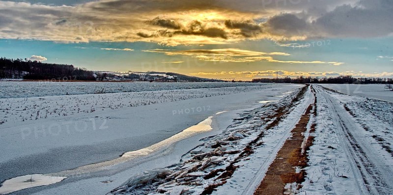 Field path with snow and sun behind clouds