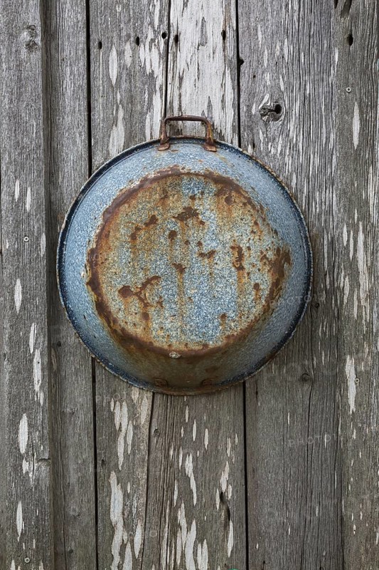 Old rusted pan hanging on grey weathered wall of old rustic wood plank cabin