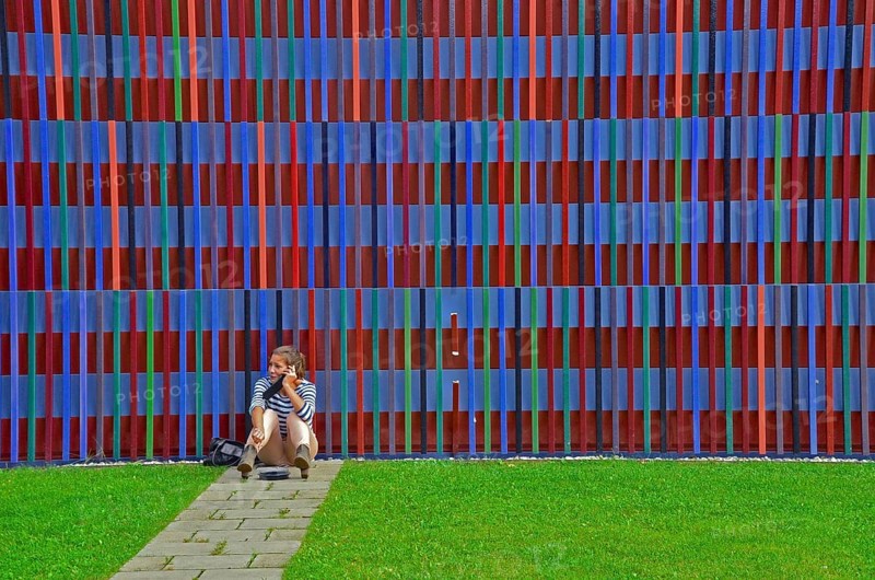 Young woman on the phone sitting on the floor in front of the colourful striped facade of the Museum Brandhorst