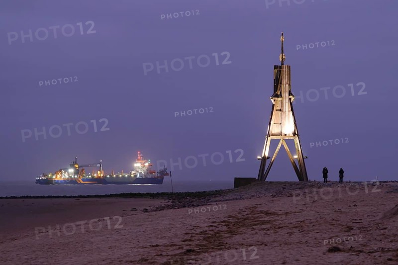 Illuminated Kugelbake and illuminated ship at blue hour