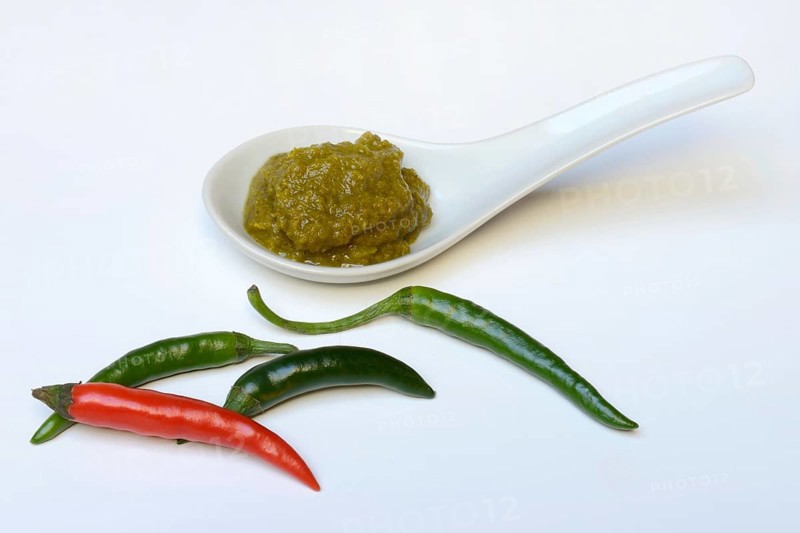 Green Thai curry paste in ceramic spoon and chillies
