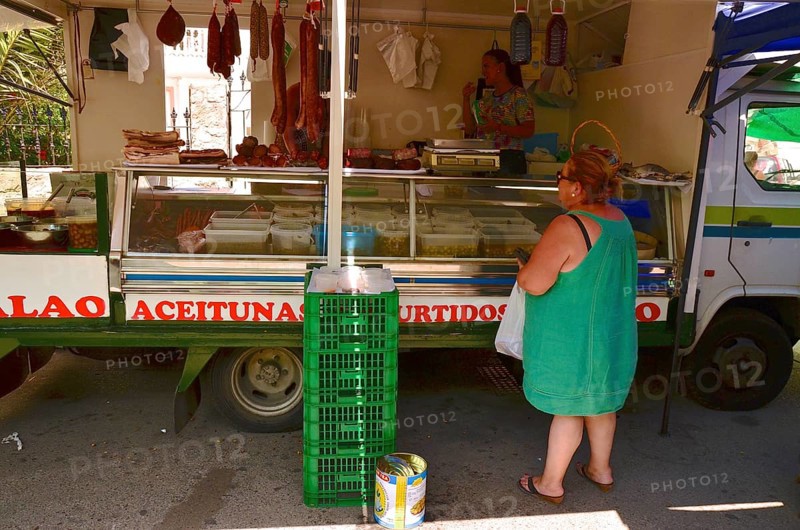 Fat woman in airy dress stands in front of sales cart with olives