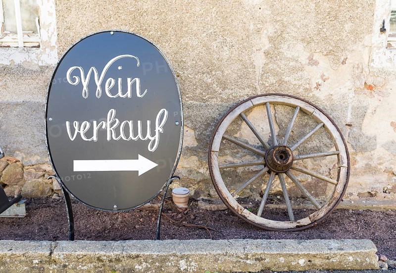 Board with arrow for wine sale and old wagon wheel as decoration at Weinhaus Schuh