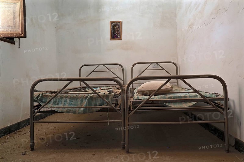 Two metal bedsteads with open window in narrow room