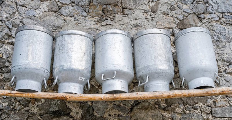 Milk cans lined up on a wooden bench