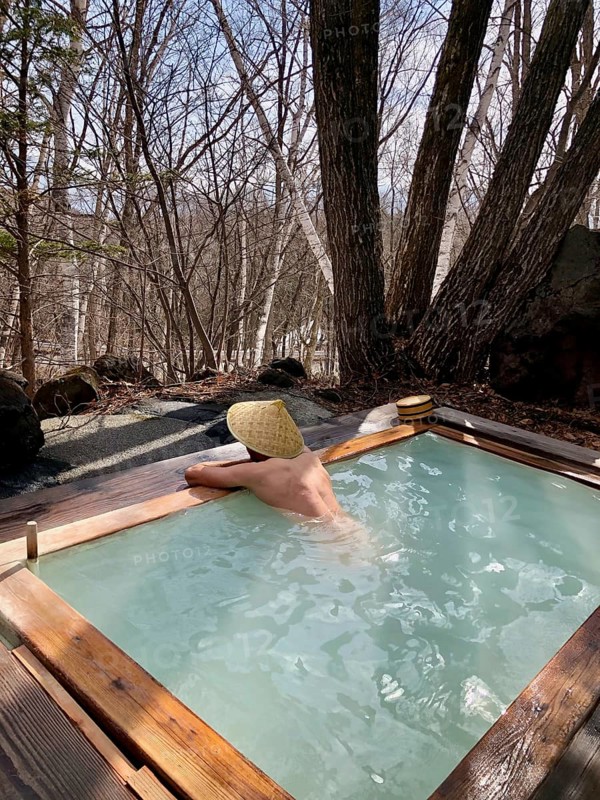 Young man with Japanese hat bathes in an onsen