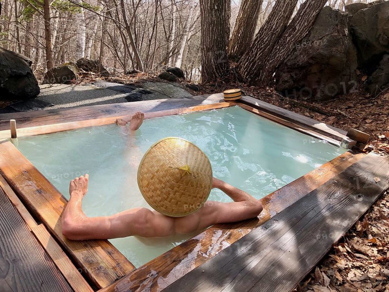 Young man with Japanese hat bathes in an onsen