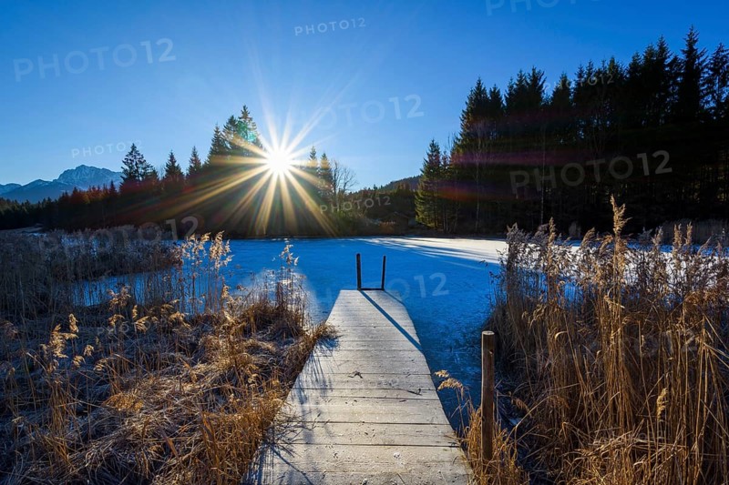 Wooden jetty with frozen lake and sun
