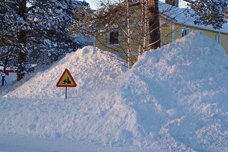 Huge snow piles and traffic sign with snowmobile in front of residential buildings