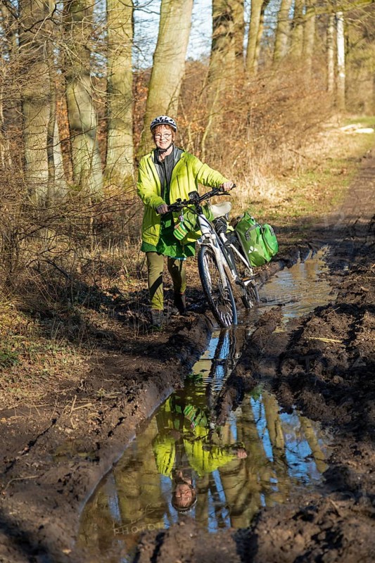 Woman cycling with e-bike over muddy forest path and through puddles